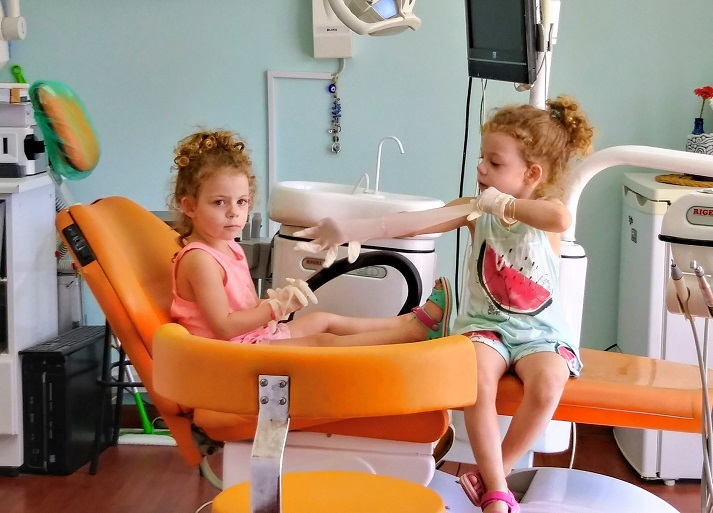 Paediatric Dentistry image showing two young children sitting on the dental chair playing with rubber examination gloves.